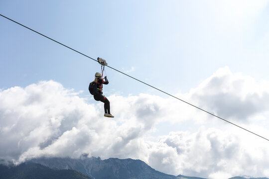 Woman on zipline harness helmet mountain background cloudy sky extreme sport adrenaline outdoor altitude thrill