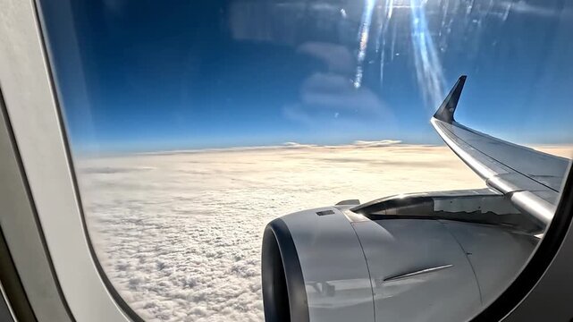Airplane wing and engine visible from window flying above f clouds with bright