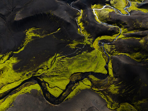 Aerial view of stark, dark volcanic sands interwoven with vibrant green moss and glacial streams, creating an otherworldly tapestry of textures and tones, Iceland.