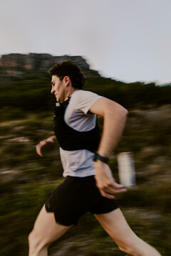 Side view of trail runner sprinting with motion blur effect across rugged mountain terrain. Concept of speed, endurance and high-performance outdoor running.