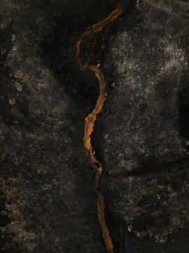 Aerial view of a fiery orange river snaking through a stark, charcoal landscape, a dramatic tapestry of nature's artistry, Rangarthing eystra, Iceland.