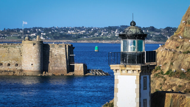 Aerial view of a lighthouse standing proudly against the rugged coastline, juxtaposed with the formidable Chateau du Taureau, Plouezoc'h, Bretagne, France.