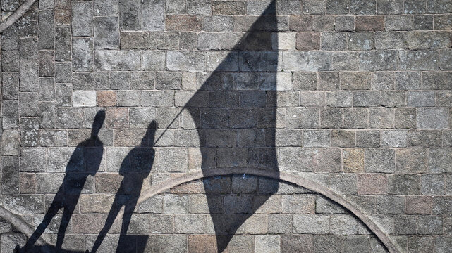 Aerial view of stark shadows cast by figures and a flag against the textured stone wall of Barnenez Cairn, Plouezoc'h, Bretagne, France.