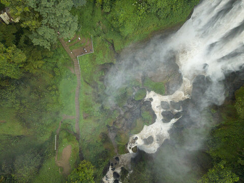Aerial view of water plunging down into a misty abyss besides lush green vegetation, Curugsewu, Kendal Regency, Central Java, Indonesia.
