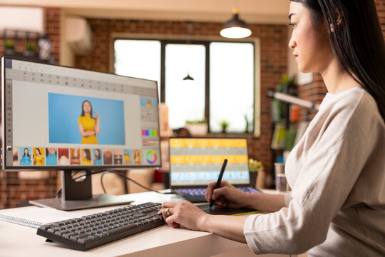 Talented graphic editor adjusts design features and retouches images using drawing tablet. Asian female photographer updating portfolio, working precisely on visual content from home studio.