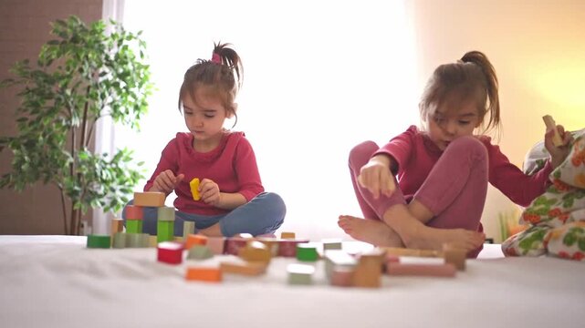 Little twin sisters playing with colorful wooden building blocks