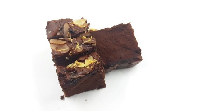 Rich dark chocolate almond fudge brownies are stacked and presented in implied motion against a stark white background for a delicious food clip.