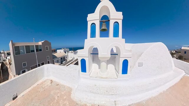 White Greek Orthodox church with a bell tower and blue accents, overlooking Santorini Aegean Sea in Greece. A sign reminds visitors not to climb on the holy place.