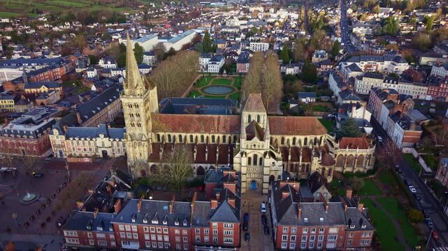 Drone rising above Saint Peter Cathedral revealing town square fountain, surrounding streets and historic center of Lisieux in Normandy France.