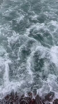 Mesmerizing slow motion top view of powerful ocean waves crashing and churning. Beautiful dynamic white sea foam and splashing water creating an abstract marine nature background.
