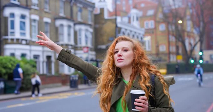 Redhead woman with coffee hailing taxi on a London street
