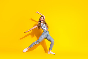 Cheerful young woman dancing joyfully against a vibrant yellow background, showcasing casual...