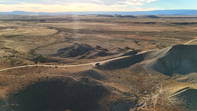 Aerial view of a lone vehicle threading through the undulating, sun-baked terrain, a stark contrast between the vehicle's dark silhouette and the ochre landscape, Fruita, Colorado, United States.