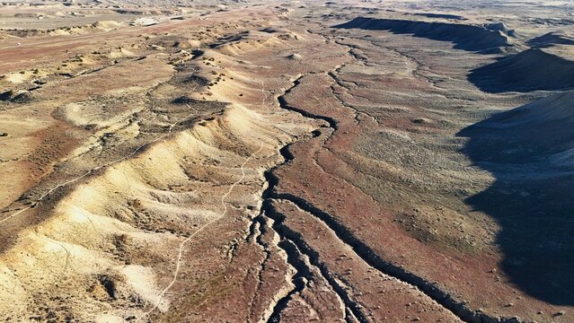 Aerial view of rugged terrain carved by deep ravines, where earthy tones meet the vast expanse of the arid landscape, Fruita, Colorado, United States.