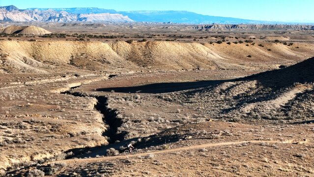 Aerial view of a lone cyclist navigates the arid landscape, carving a path through the rugged terrain under the vast sky, Fruita, Colorado, United States.