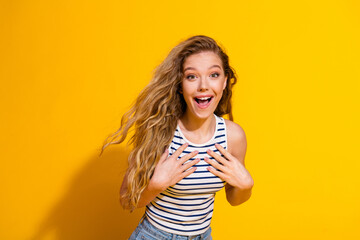 Cheerful young woman expressing excitement with her hands on chest against vibrant yellow...