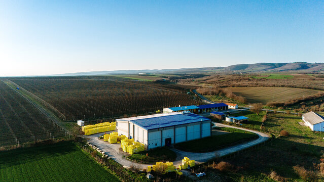 Aerial view of the industrial building gleaming under a clear sky, surrounded by verdant fields and distant hills, a blend of modern structure and natural beauty, Jazak, Vojvodina, Serbia.