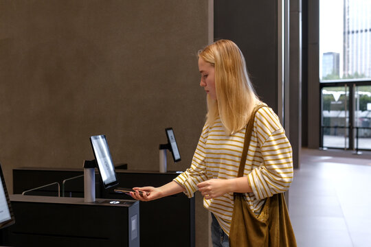 Contactless check-in with smartphone at self-service access kiosk in modern office lobby, Gen Z hybrid work and smart building security concept, copy space.