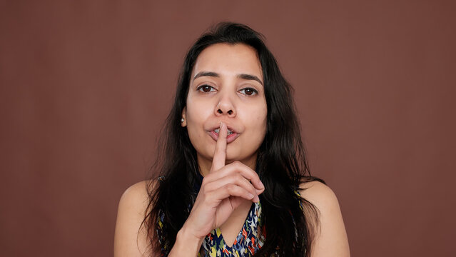 Secretive adult keeping secret with mute and silence sign, holding finger over mouth. Confidential private information doing hush gesture, not sharing unbelievable rumor and gossip.