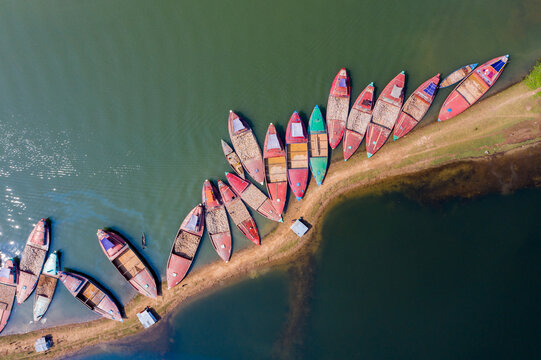 Aerial view of colourful boats nestled along the sandy shores, contrasting with the dark waters, creating a striking tapestry of vibrant hues, Barek Tila, Sylhet Division, Bangladesh.