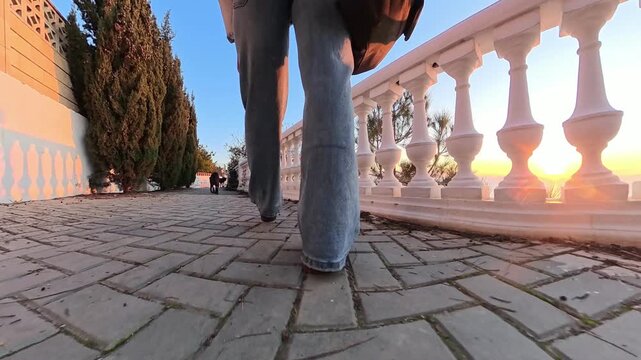 Walking promenade sunset person in jeans walks along a white balustrade walkway during a bright golden hour