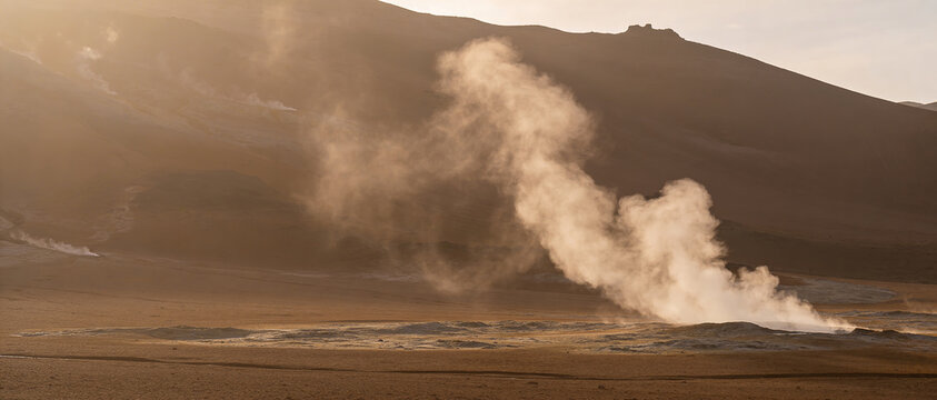Steaming fumaroles in rocky valley against majestic dark mountains.