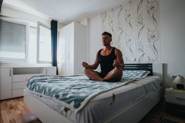 A man sits cross-legged on a bed meditating in a bright bedroom at home. The scene shows a calm...