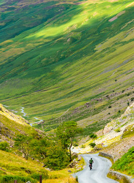 A bicycle rider peddles into Honister Pass,along a narrow,winding road,the Lake District,Cumbria,England,United Kingdom.