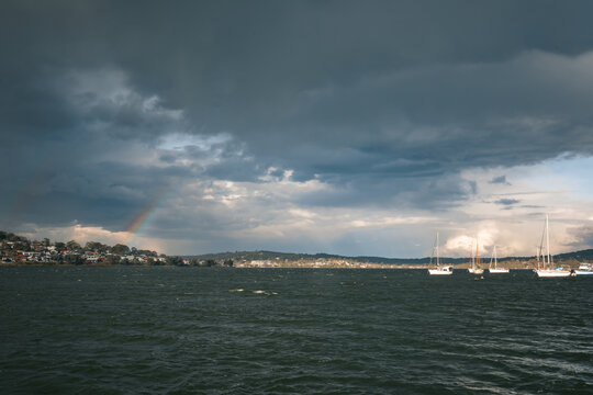 Dramatic storm clouds passing over lake with sailboats and a faint rainbow appearing