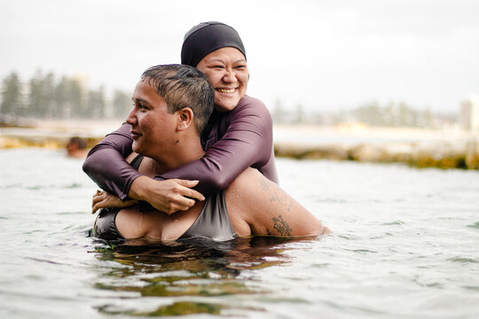 Hmong-American woman riding on piggyback of French Islander woman inside tidal pool