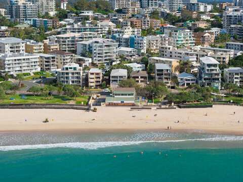 Distant aerial view of turquoise ocean lapping onto a city beach in front of waterfront apartments