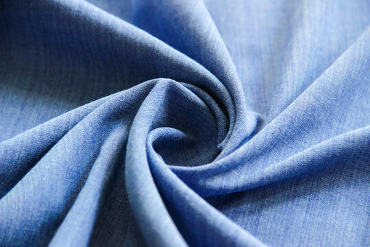Blue fabric arranged in a spiral fold, showcasing smooth texture and elegant drapery. Ideal for textile, fashion, and abstract background concepts