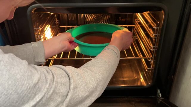 Horizontal video: side and slightly top view, placing turquoise round silicone mold with batter into the oven for cake preparation.