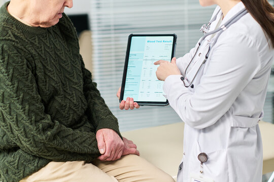 Adult man sitting while female doctor showing blood test results on digital tablet, medical professional explaining health information during consultation