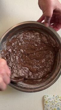 Top view vertical video of dark cake batter being mixed with a spoon in a metal bowl, creamy sour cream-like consistency, homemade baking process