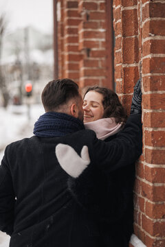 Happy couple in warm clothes embracing near brick wall on city street in winter  