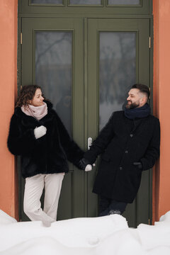 Happy couple in stylish winter clothes holding hands and looking at each other in city street 