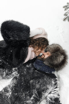 High angle of couple in love kissing while lying on snowy ground in winter forest  