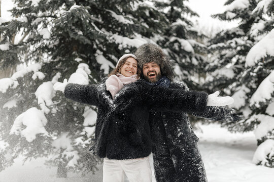 Carefree couple with stretched arms having fun in snowy winter park 