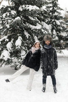 Full length of content couple wearing warm winter clothes standing in snowy park and having fun 
