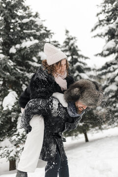 Low angle of positive couple enjoying piggyback ride during date in snowy winter park  