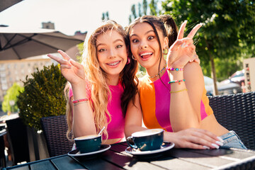Two stylish young friends pose at sunny outdoor cafe enjoying a fun day in the city