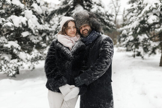 Happy couple wearing warm coats holding hands while standing in snowy winter park 