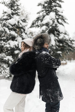 Stylish couple in winter clothes standing back to back together in snowy park