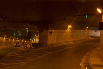 Tunnel maintenance area with traffic cones, temporary barriers, directional markings, dim lighting and lone vehicle turning, © Alena