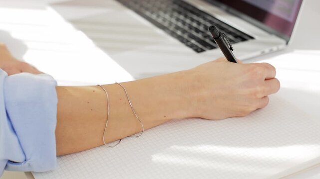 female hand writing in notebook for planning or reminding herself of tasks. close-up. student with laptop for education. female worker takes notes