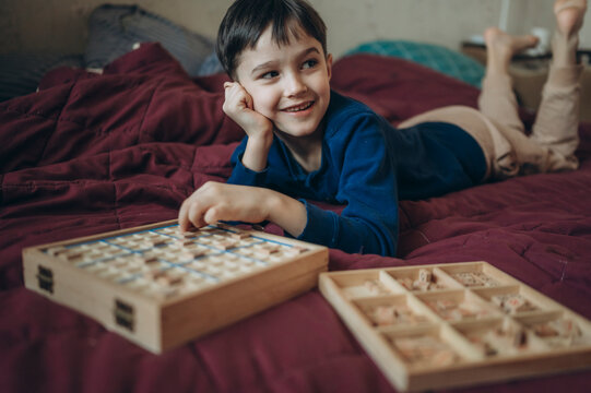 Child lying on bed playing Sudoku puzzle board game at home