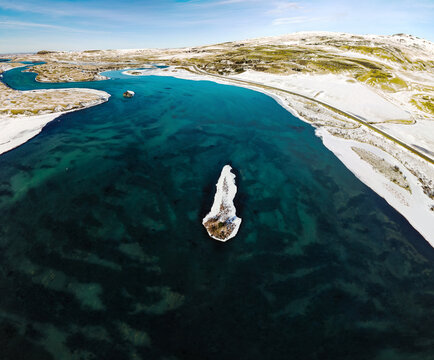 Aerial view of the cold turquoise sea contrasting with the crisp white snow-covered land, creating a serene and stark landscape, Iceland.