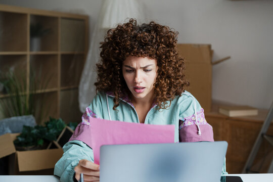 Confused woman reading documents while working from home at desk