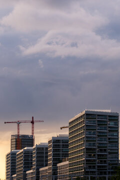 Urban city skyline in Berlin Germany showing modern building silhouettes at soft dusk with a distant crane under wide cloud filled sky